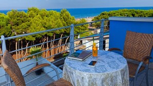 A balcony with wicker chairs, a round table, and a view of the sea and beach. - Hotel Antares (Alba Adriatica)