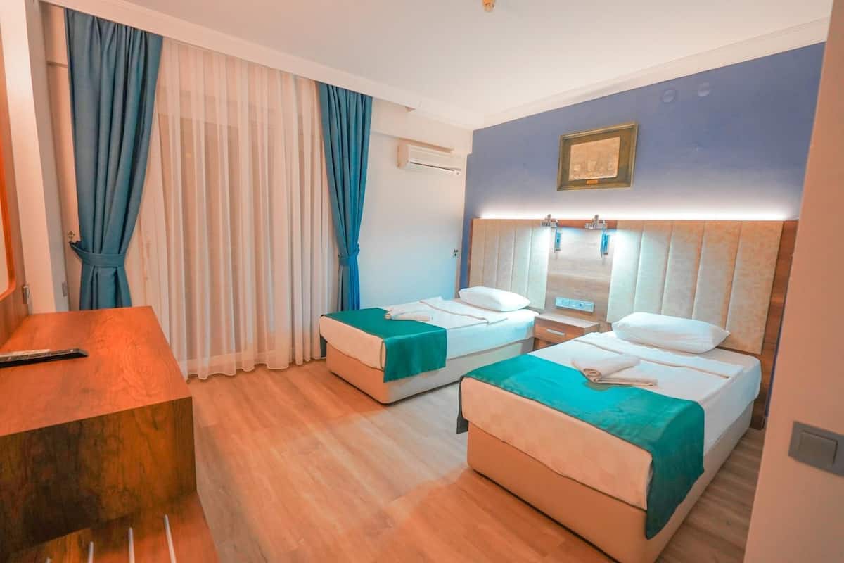 A hotel room with two beds, a desk, and a large window with curtains.