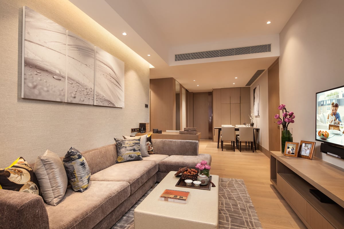 A modern living room with a sectional sofa, a coffee table with decorative items, a flat-screen TV, and a dining area with a table and chairs.