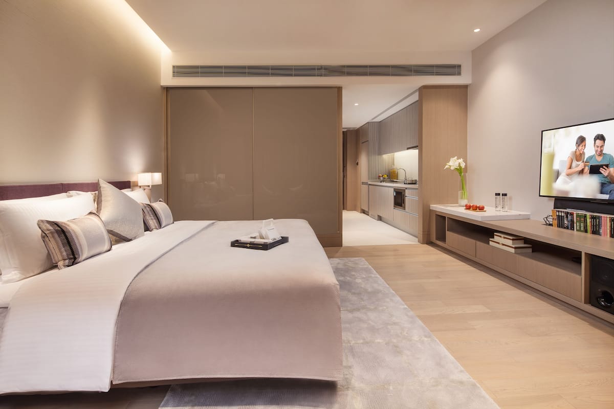 A modern hotel room with a large bed, a TV, a small kitchenette, and a sliding door closet.