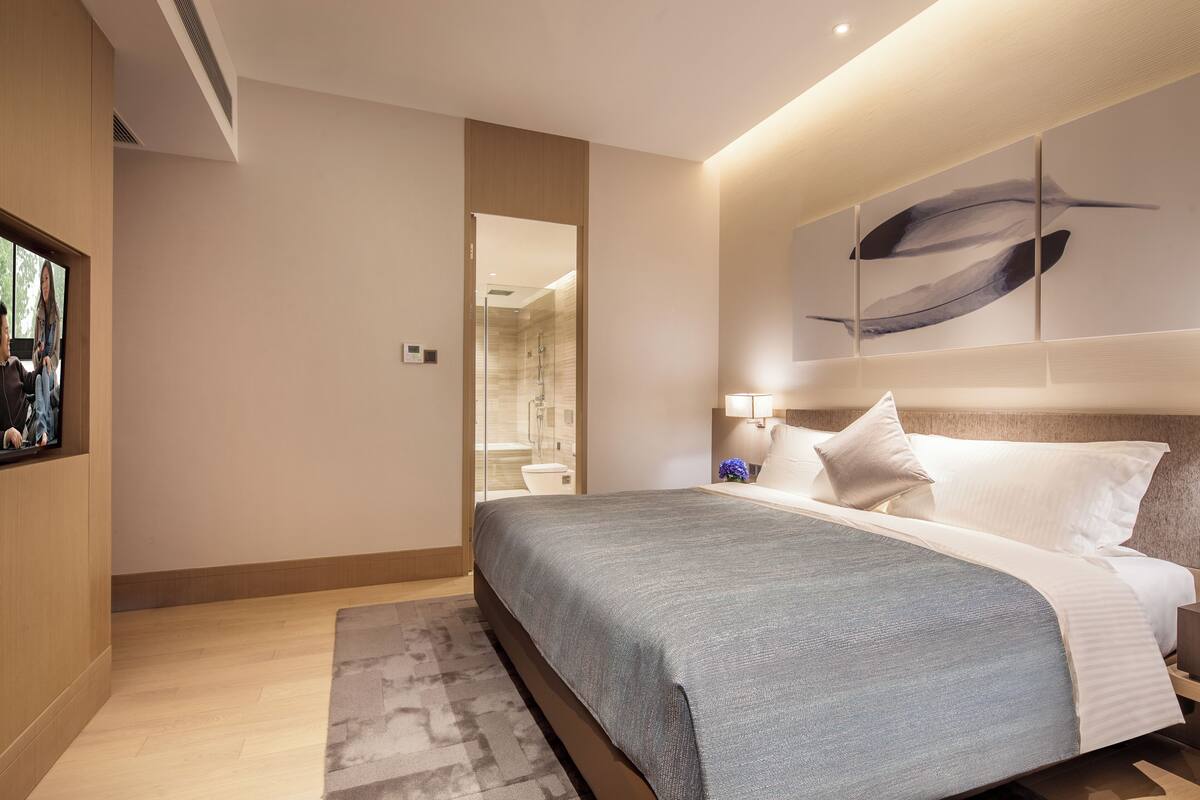 A modern hotel room with a large bed, a flat-screen TV, and a bathroom visible through an open door.