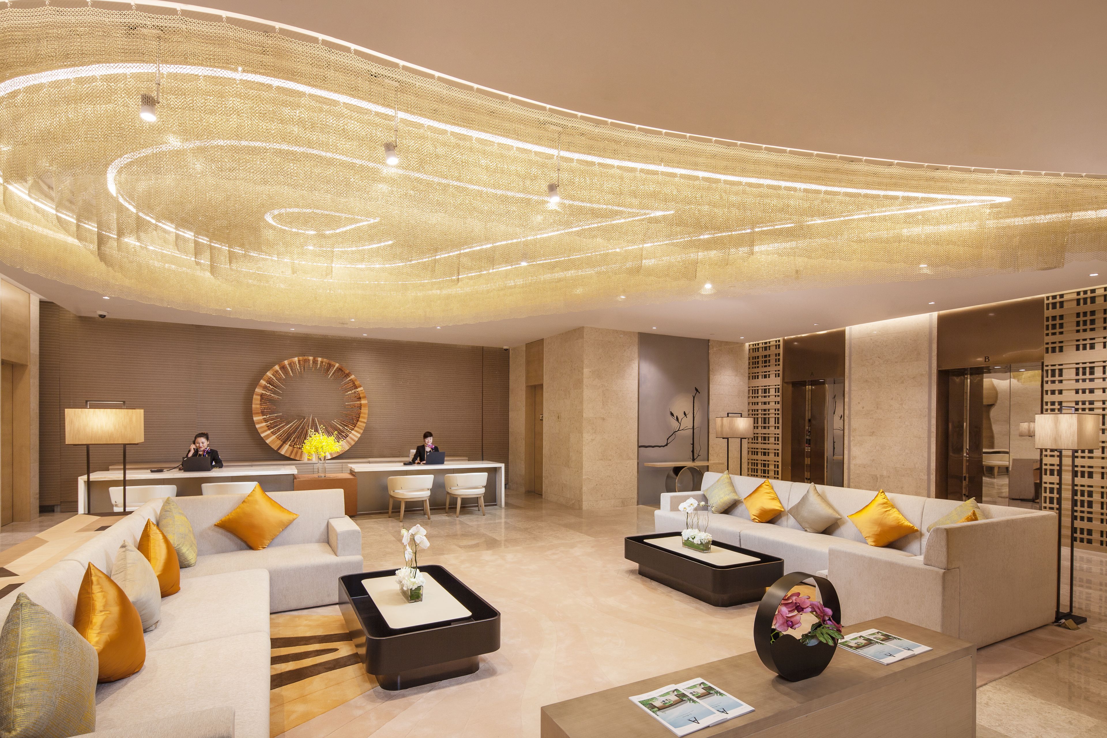 A modern hotel lobby with a reception desk, seating area, and decorative lighting.