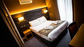 A hotel room with a large bed, bedside lamps, a desk, and a window with curtains.
