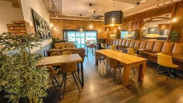 A cozy restaurant with wooden tables and chairs, a large plant, and a modern ceiling design.