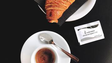 A croissant on a white plate with a napkin, a spoon, and a small cup of coffee on a black table.