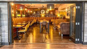 Un bar restaurante con cabinas de cuero, mesas de madera y un ambiente cálido.