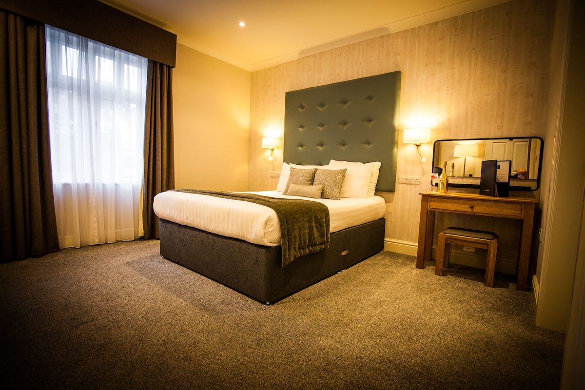 A hotel room with a large bed, a bedside table, a mirror, and a lamp.