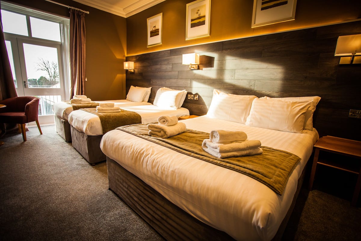 A hotel room with two beds, a chair, and a view of the outdoors.