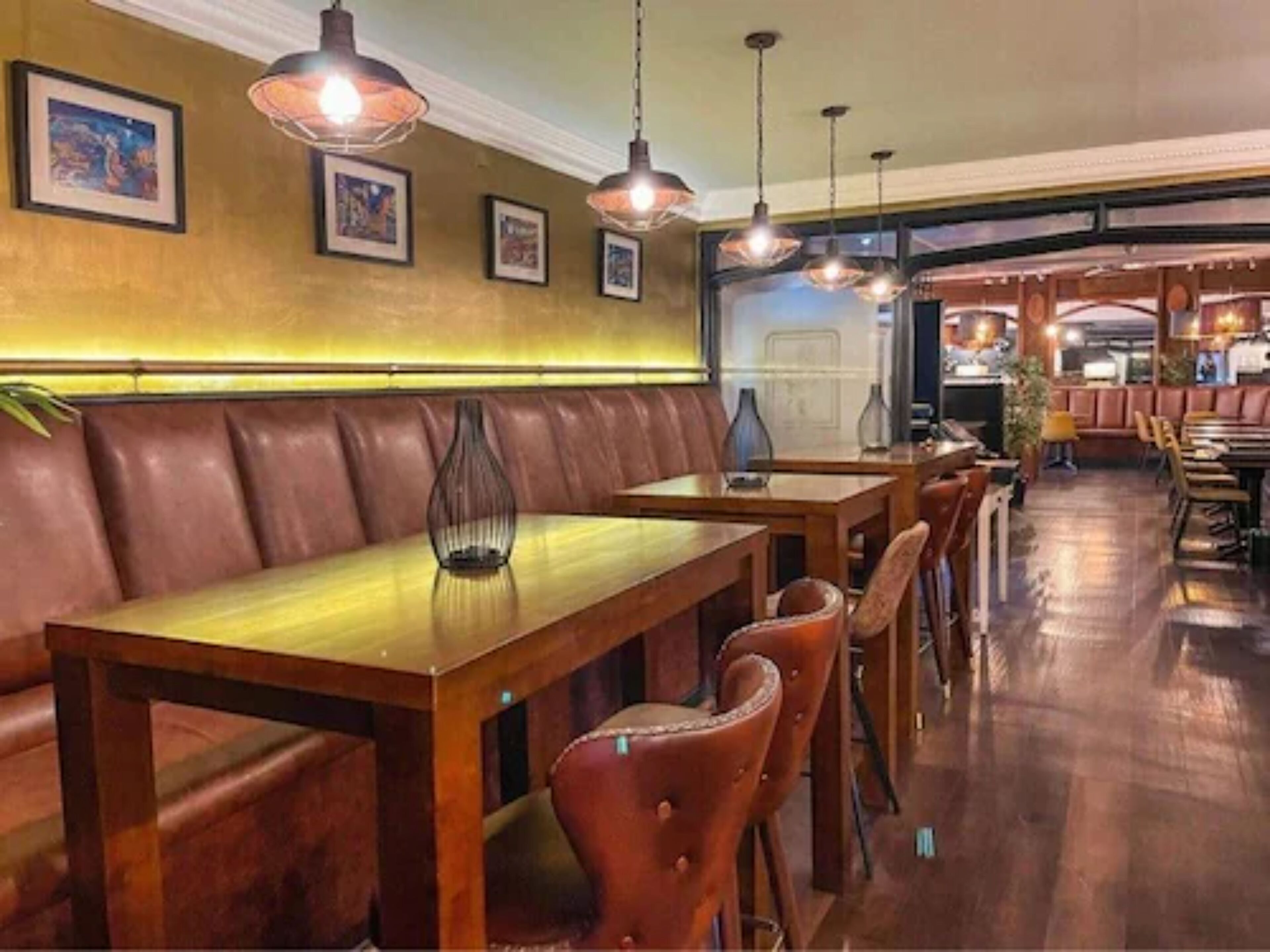 Een restaurant interieur met houten tafels en lederen zithoeken, hanglampen, lijstwerken aan de muren en zicht op de eetzaal.