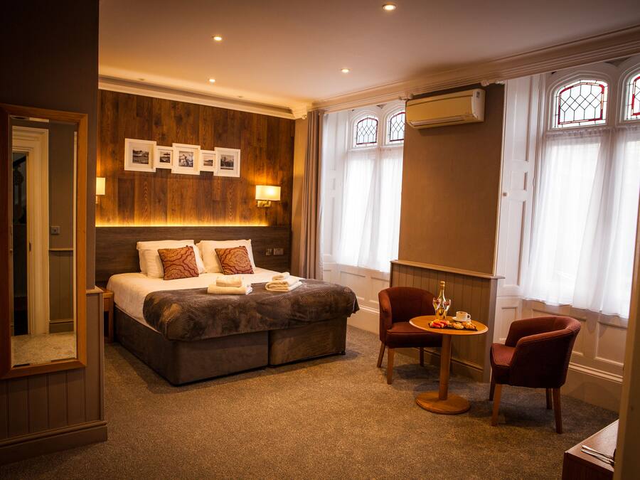 Una habitación de hotel con una cama grande, una zona de estar con mesa y sillas, y un ventanal con cortinas.