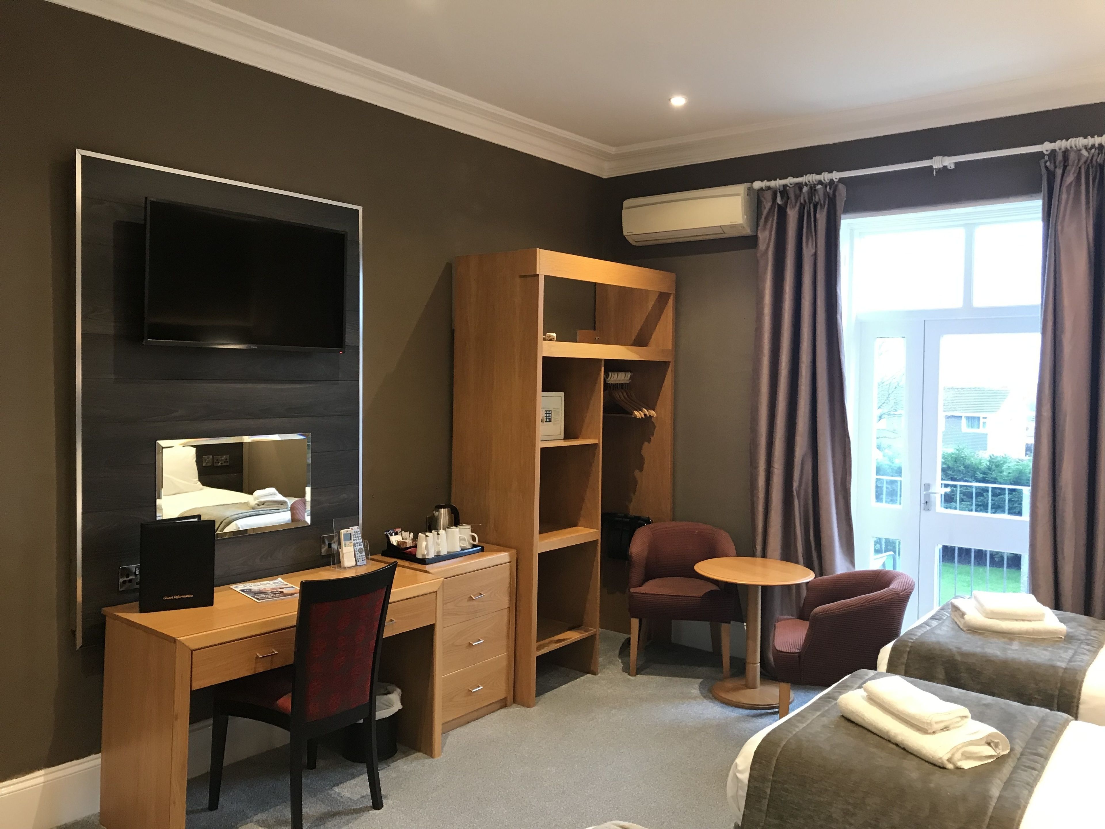 A hotel room with a desk, chair, two beds, a TV, a wardrobe, and a window with curtains.