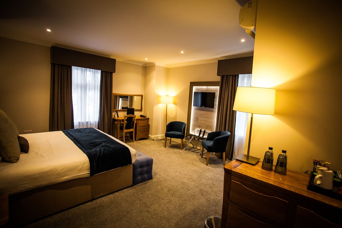 A hotel room with a bed, desk, chair, and a lamp.