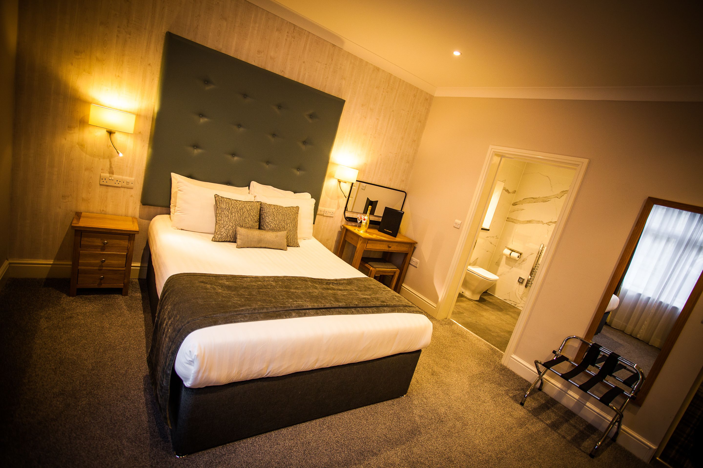 Una habitación de hotel con una cama grande, una mesita de noche, una silla y un baño visible a través de una puerta abierta.