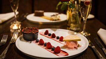 A dessert plate with strawberries and a chocolate dish, a glass of wine, and a rose in the background.