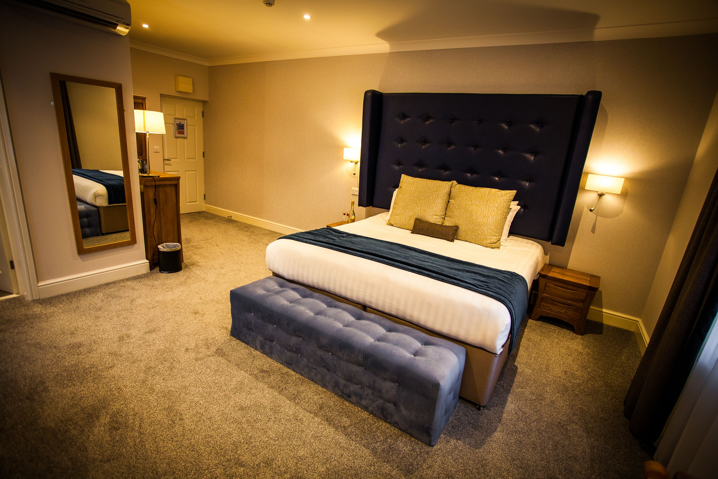 A bedroom with a large bed, a bench, a mirror, and two bedside lamps.