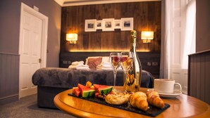 Una habitación de hotel con una cama, una mesita de noche con una bandeja de comida, una botella de champán y una taza de café.