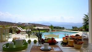 A table set with breakfast items and a view of a swimming pool and mountains. - Valea Villa (Naxos)