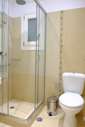 A bathroom with a glass-enclosed shower, a toilet, and a trash bin. - Valea Villa (Naxos)