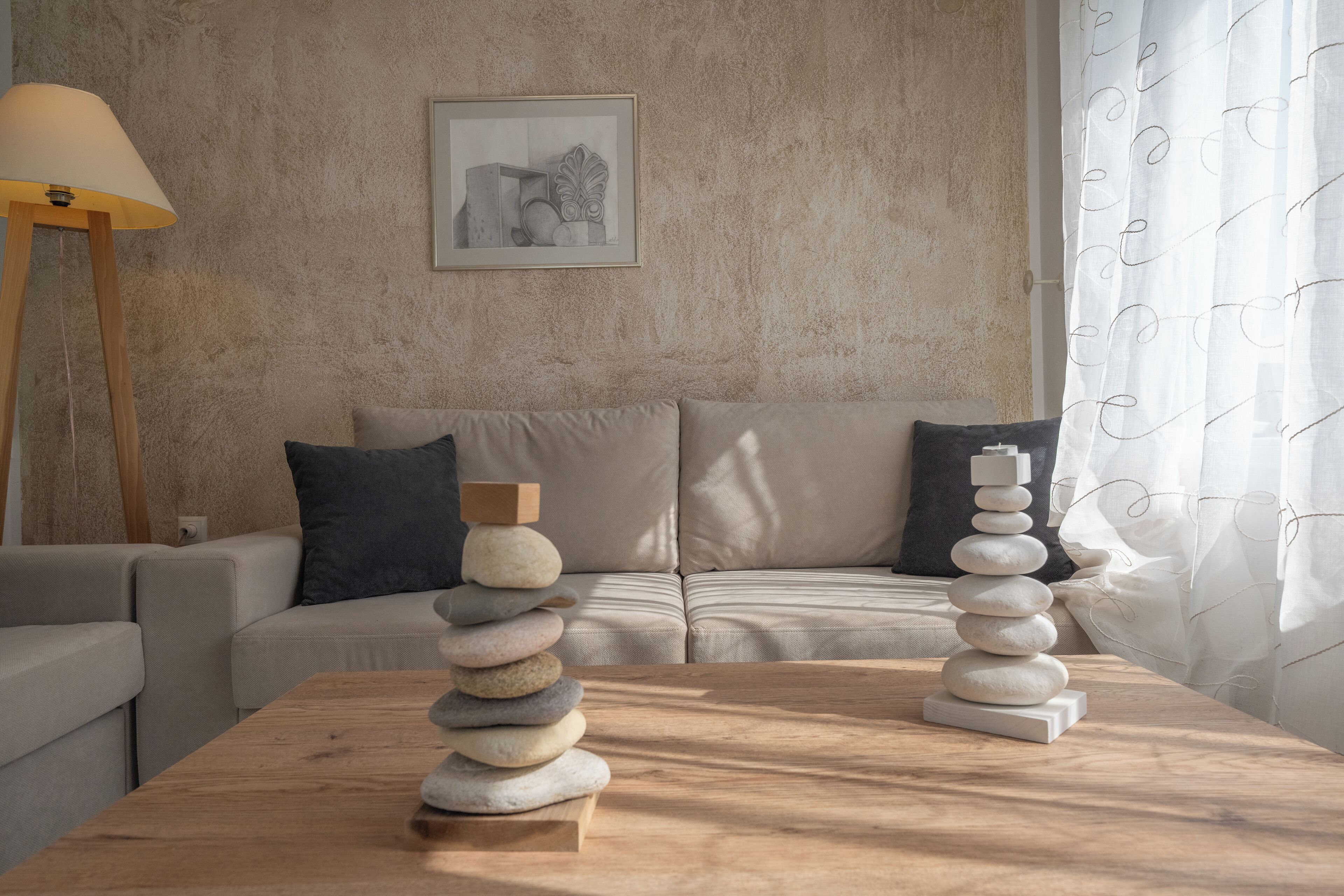 A modern living room with a wooden coffee table, a stack of stones, a sofa, and a lamp.