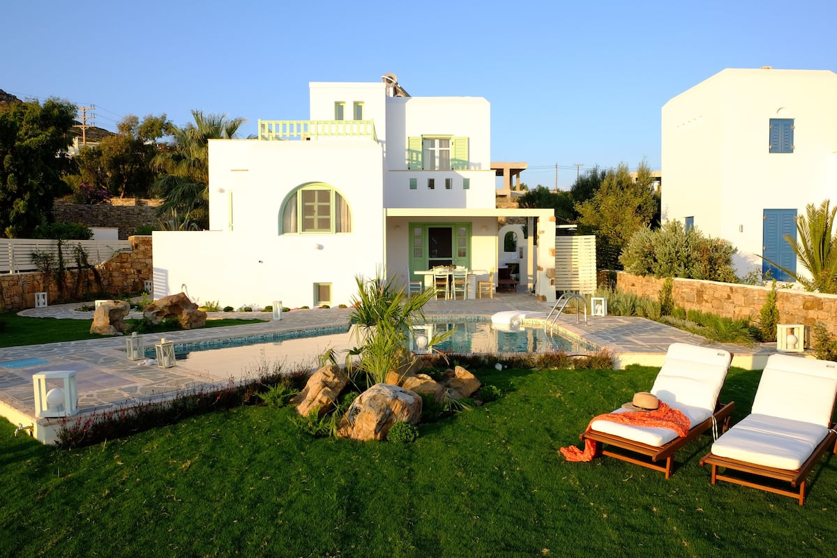 A modern house with a swimming pool, two lounge chairs, and a well-maintained garden.
