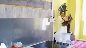 Una cocina con encimera blanca, cafetera y un florero con flores en la pared.