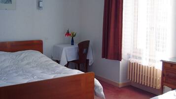 Ein Hotelzimmer mit einem Bett, einem kleinen Tisch mit Blumenvase, einem Sessel, einem Heizkörper und einem Nachttisch mit Lampe.