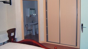 Un dormitorio con una cama, una silla de madera, un armario y un baño visible a través de una puerta abierta.