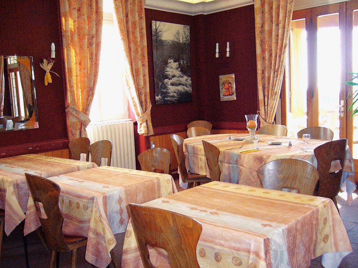 Un espace repas avec plusieurs tables et chaises, un tableau accroché au mur et une fenêtre avec des rideaux.