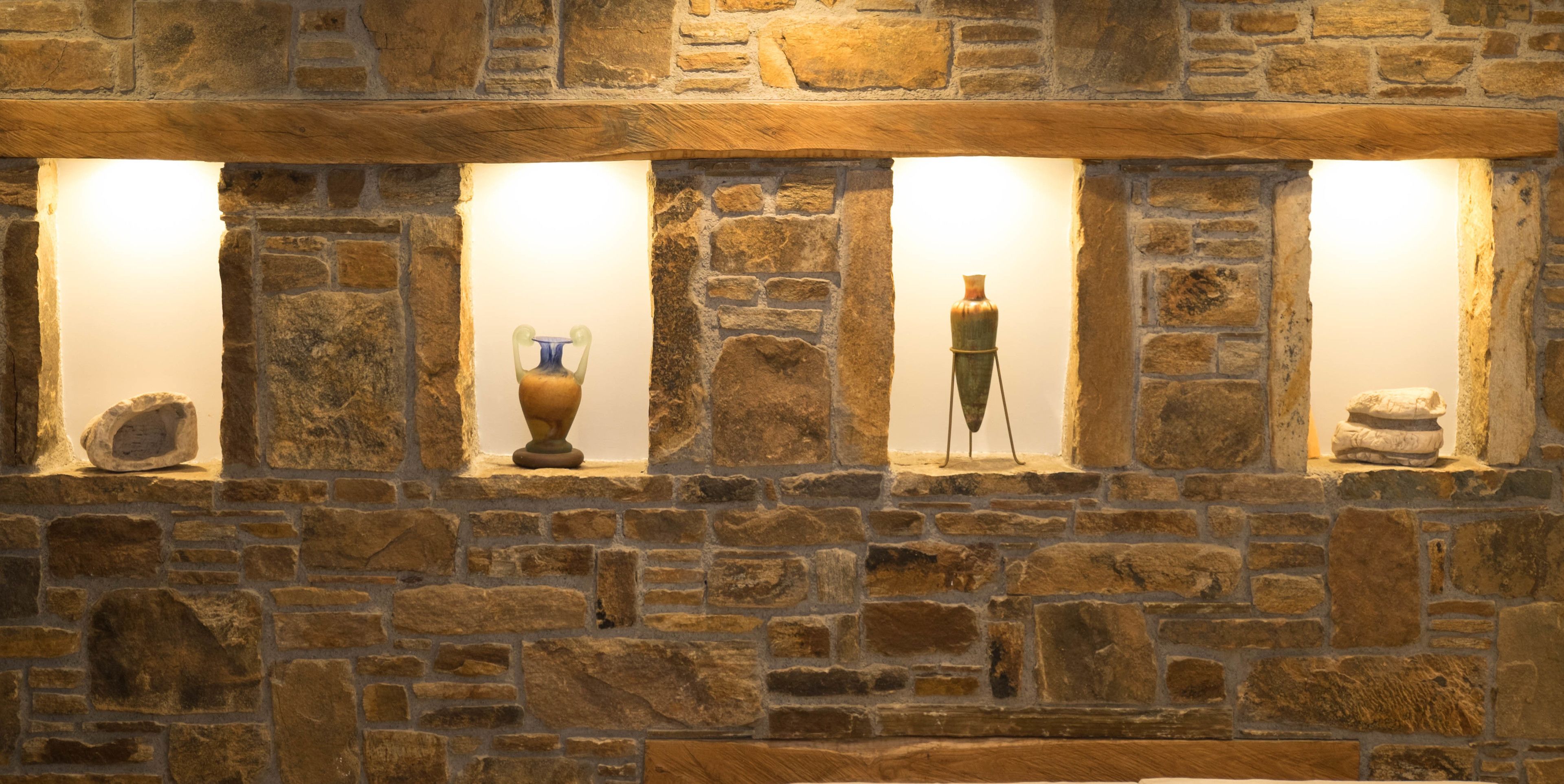A stone wall with three windows, each containing a different decorative item.