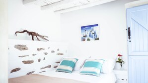 Un dormitorio con pared de piedra, una cama con almohadas a rayas, un cuadro de una escena costera y una puerta azul.