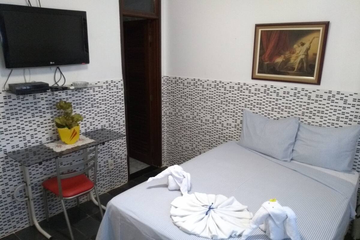 A hotel room with a bed, a desk with a chair, a television, and a painting on the wall.