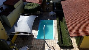 Zona de piscina en la azotea con piscina azul, tumbonas y un área de estar cubierta.