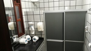 Un baño con lavamanos, espejo, dispensador de toallas y cabina de ducha.