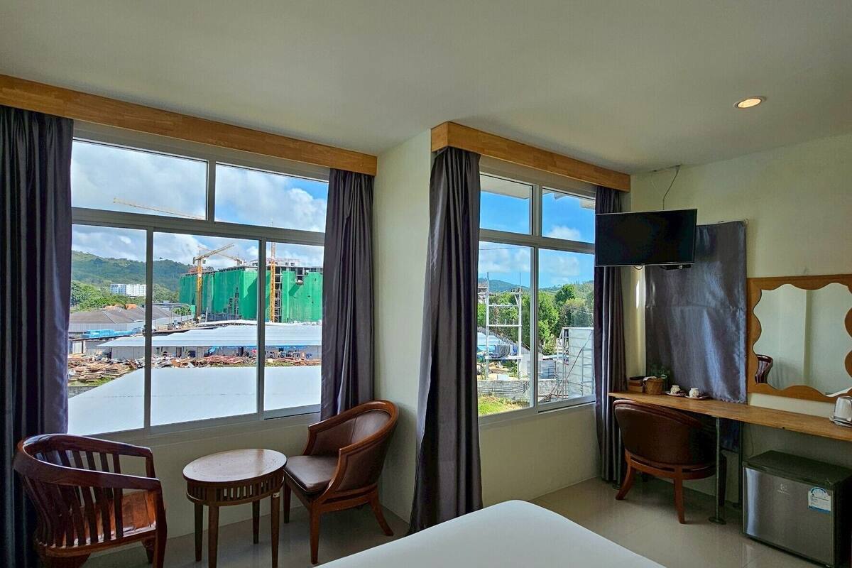 Una habitación de hotel con una cama grande, dos sillas de madera, una mesita pequeña, un televisor y un escritorio con una computadora.