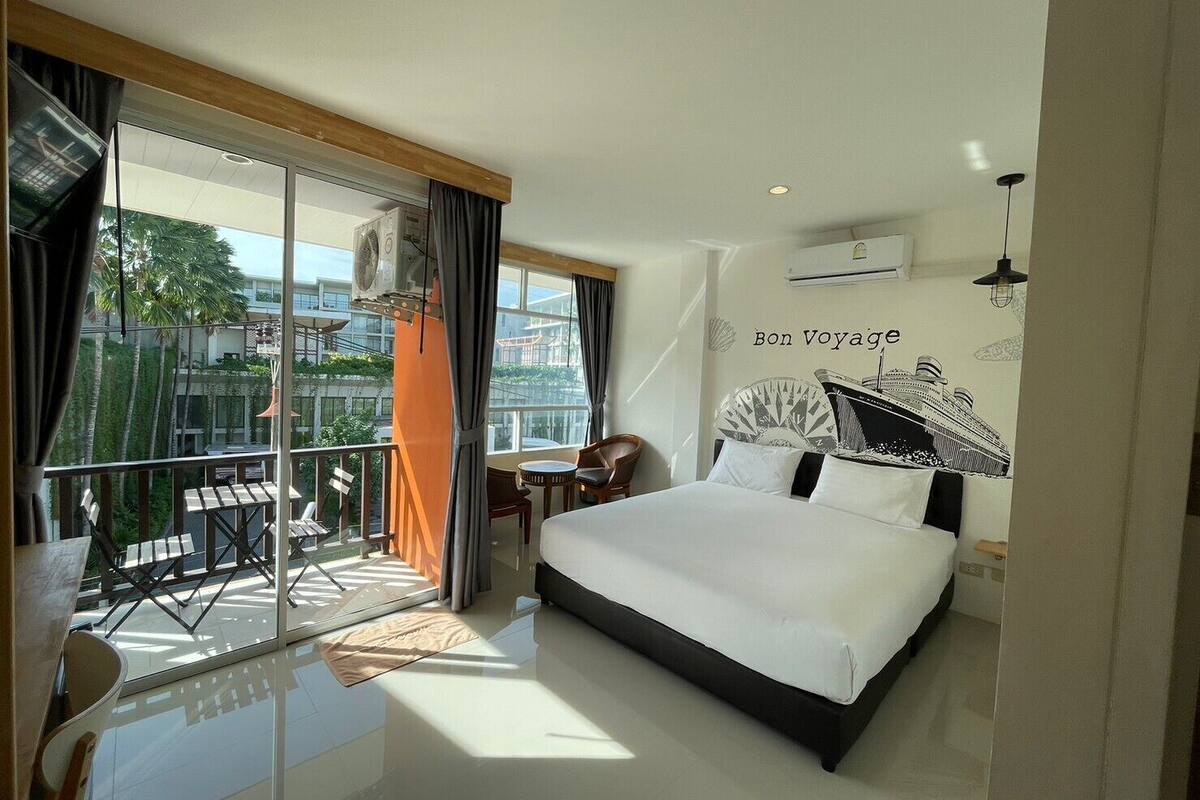Una habitación de hotel moderna con una cama grande, un balcón con mesa y sillas, y vista a la ciudad.