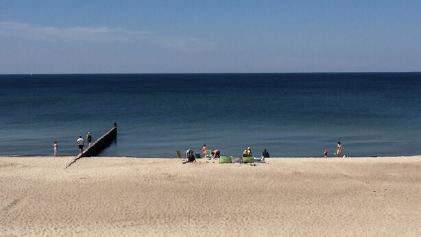 Een strand met een zandkust, enkele mensen en een rustige zee.