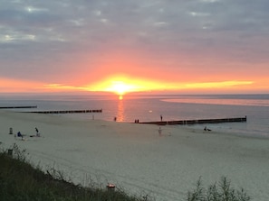 A beach with a sunset, calm sea, and a wooden pier.