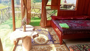 A wooden room with a bed, a small table, and a view of a green landscape. - Freedom Homestay (Ta Van)