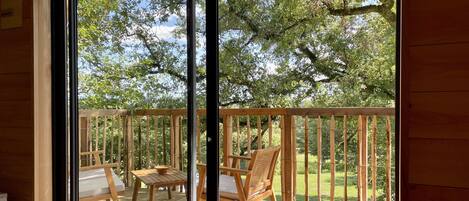 A wooden deck with a table and chairs, a large sliding glass door, and a view of a green landscape.