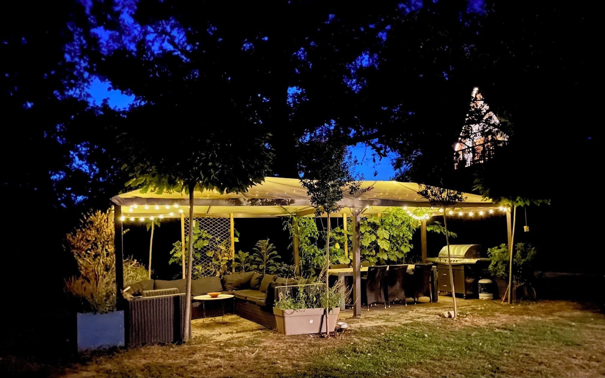 A covered outdoor seating area with string lights, a table, and chairs.