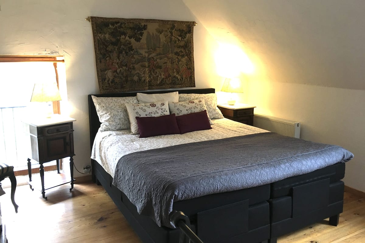 Quarto com cama, mesa de cabeceira, abajur, radiador e tapeçaria na parede.