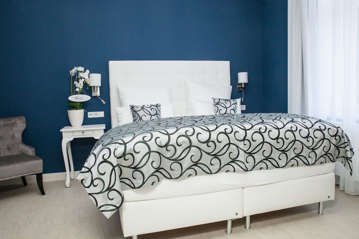 A bedroom with a white bed, a nightstand, a lamp, and a chair.