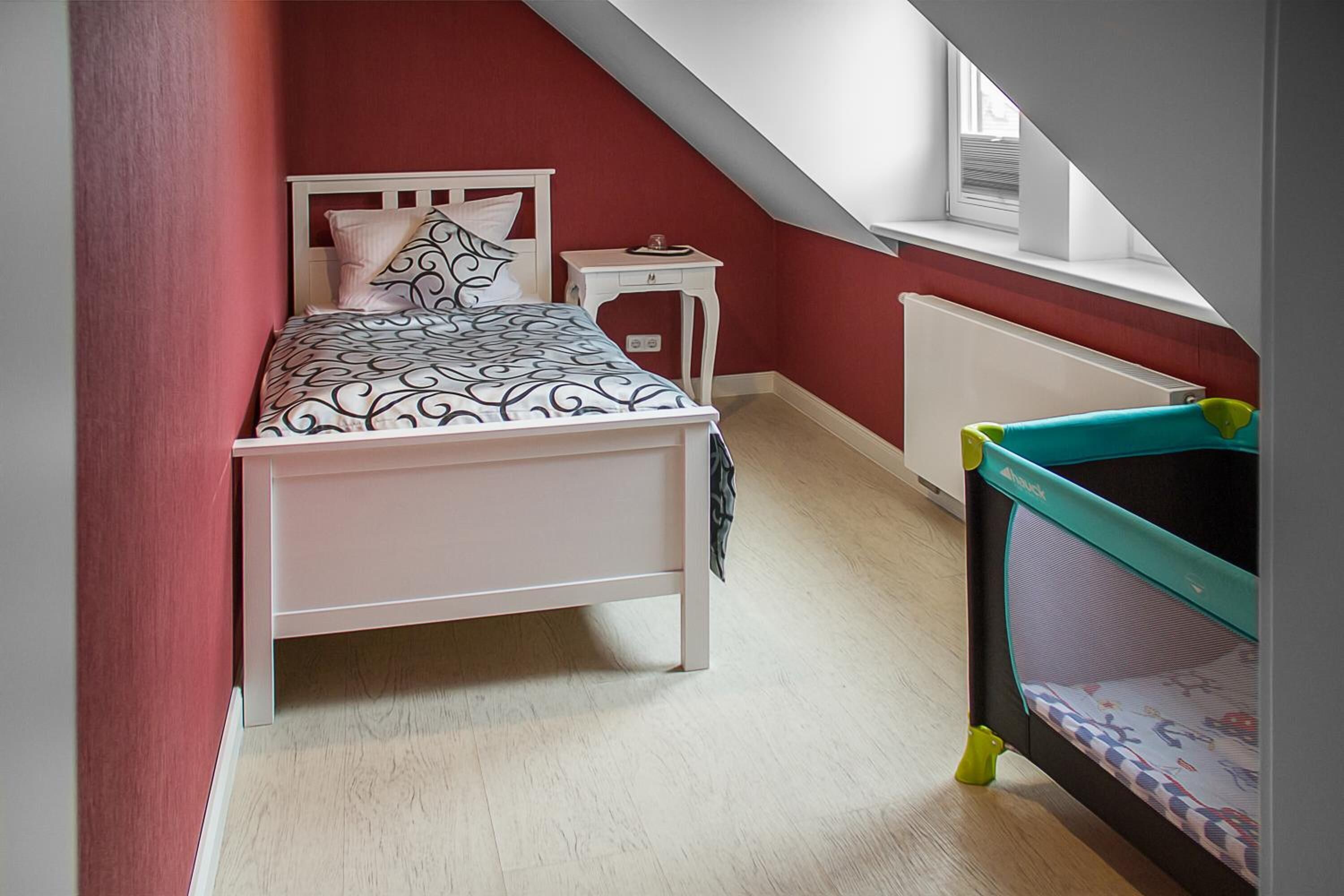 Ein Schlafzimmer mit einem Bett, einem Nachttisch, einem Fenster und einem Babybett.