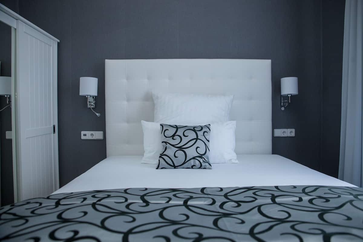 A neatly made bed with a white headboard, two bedside lamps, and a patterned bedspread.