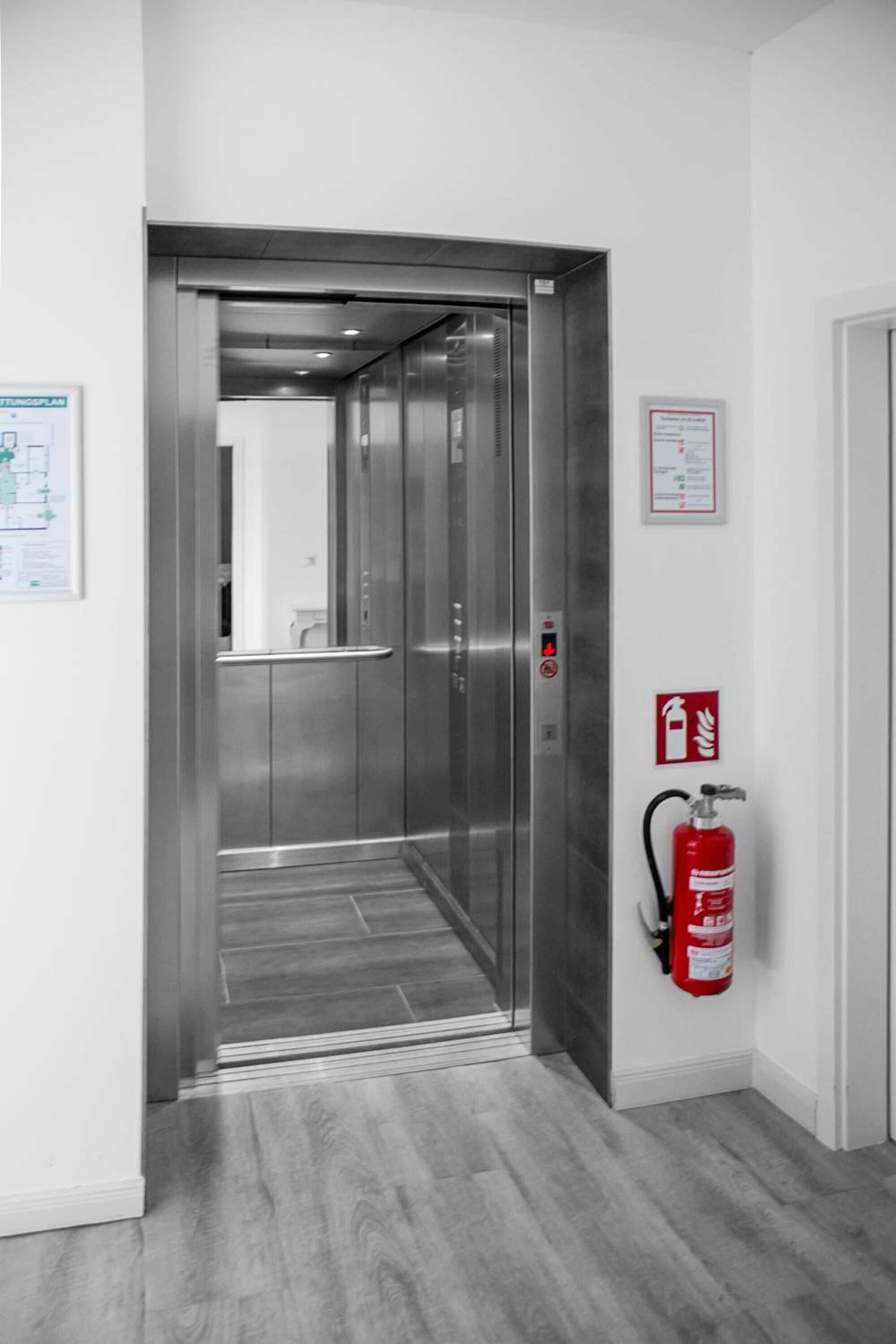 An elevator with metallic doors and a fire extinguisher mounted on the wall.