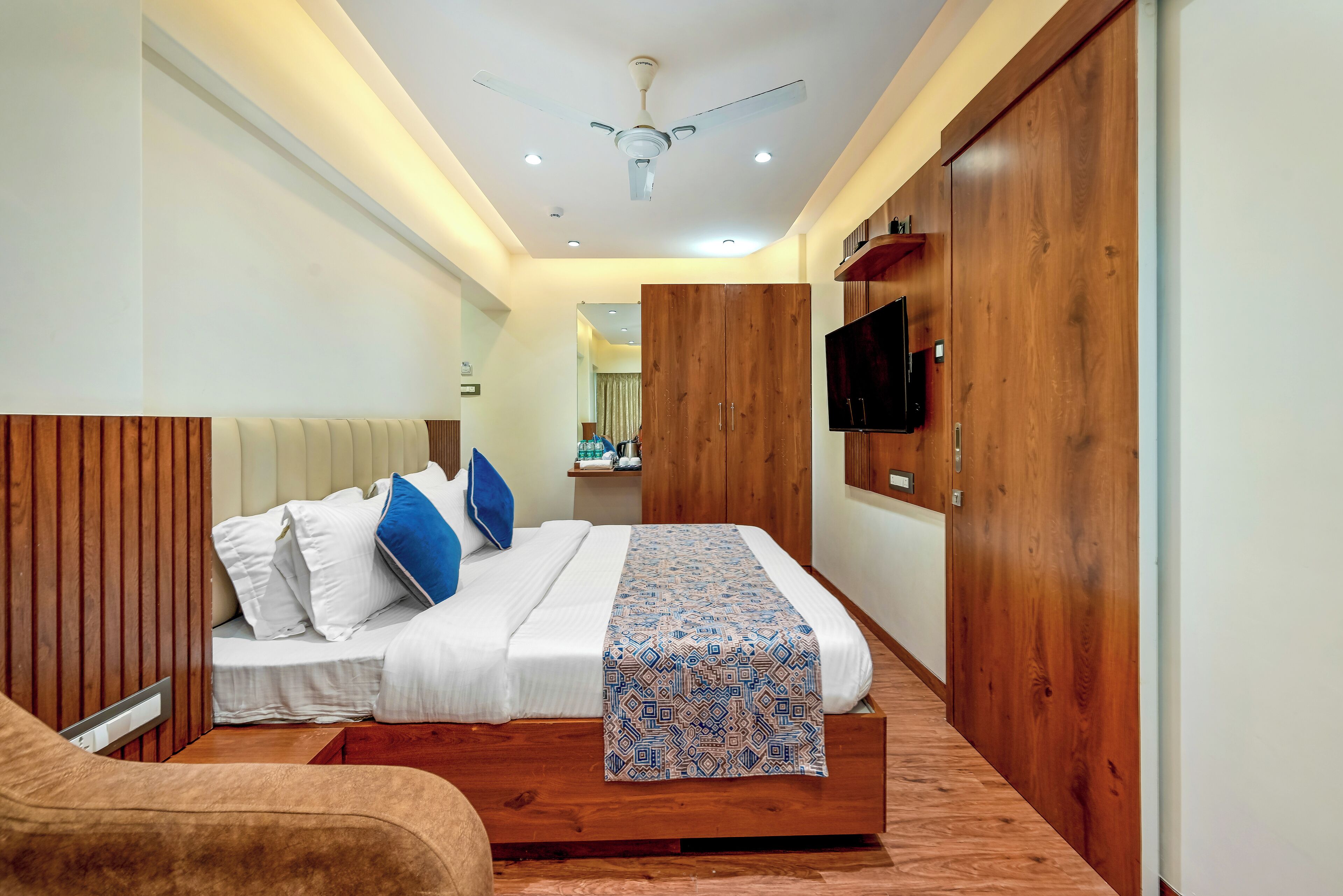 A bedroom with a bed, wooden headboard, bedside table, TV, and wardrobe.