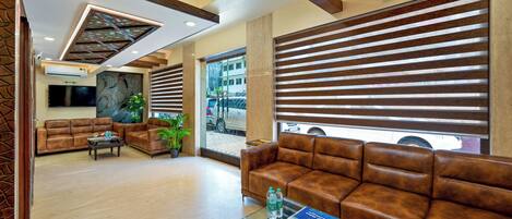 A modern lobby with leather sofas, a glass coffee table, and a large window with blinds.