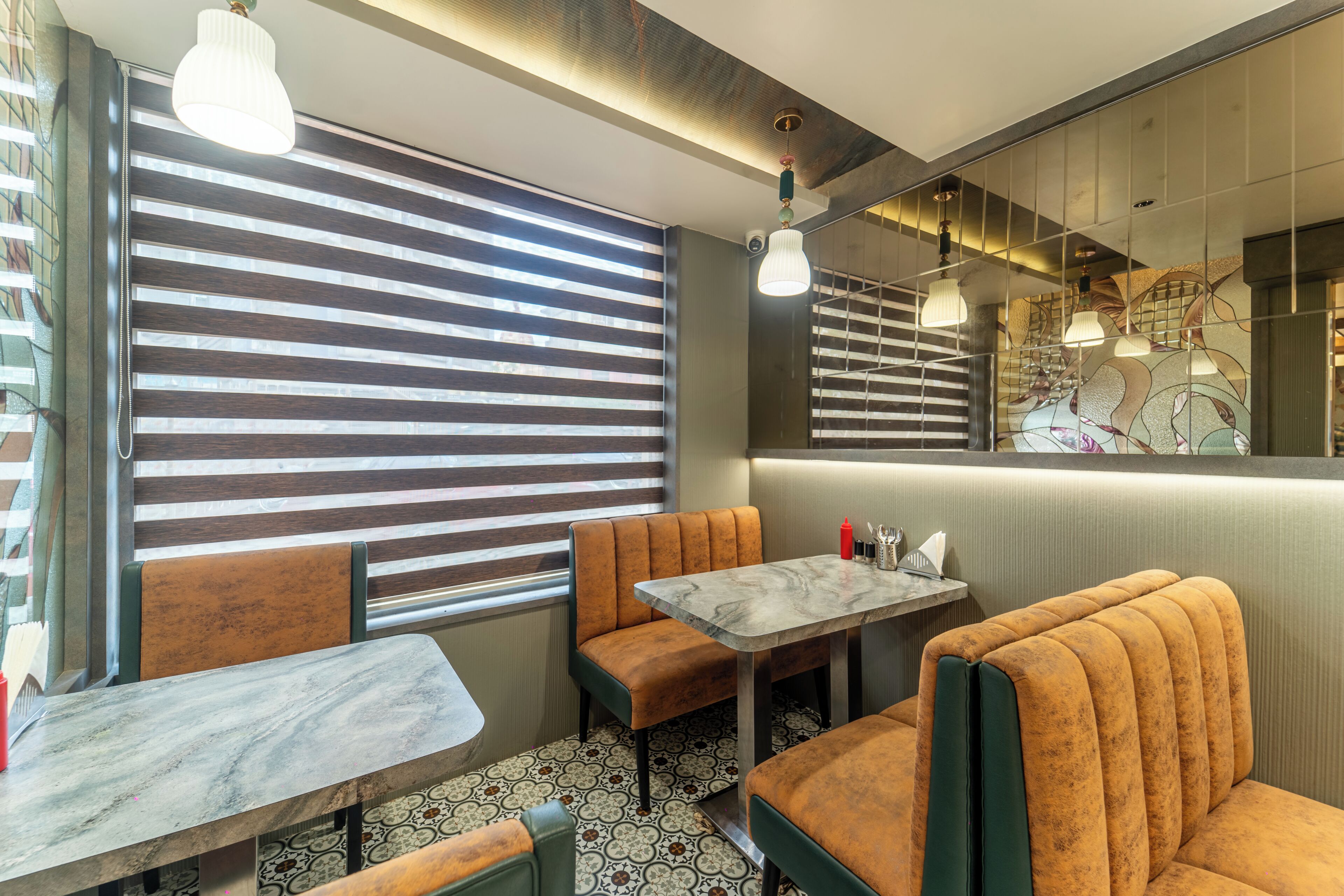 A restaurant interior with striped blinds, cushioned booths, a marble table, and pendant lighting.
