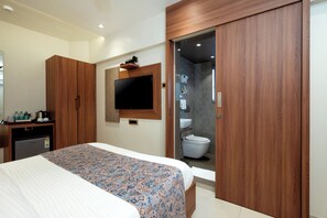 Quarto de hotel com cama, televisão, guarda-roupa e banheiro com vaso sanitário e chuveiro.