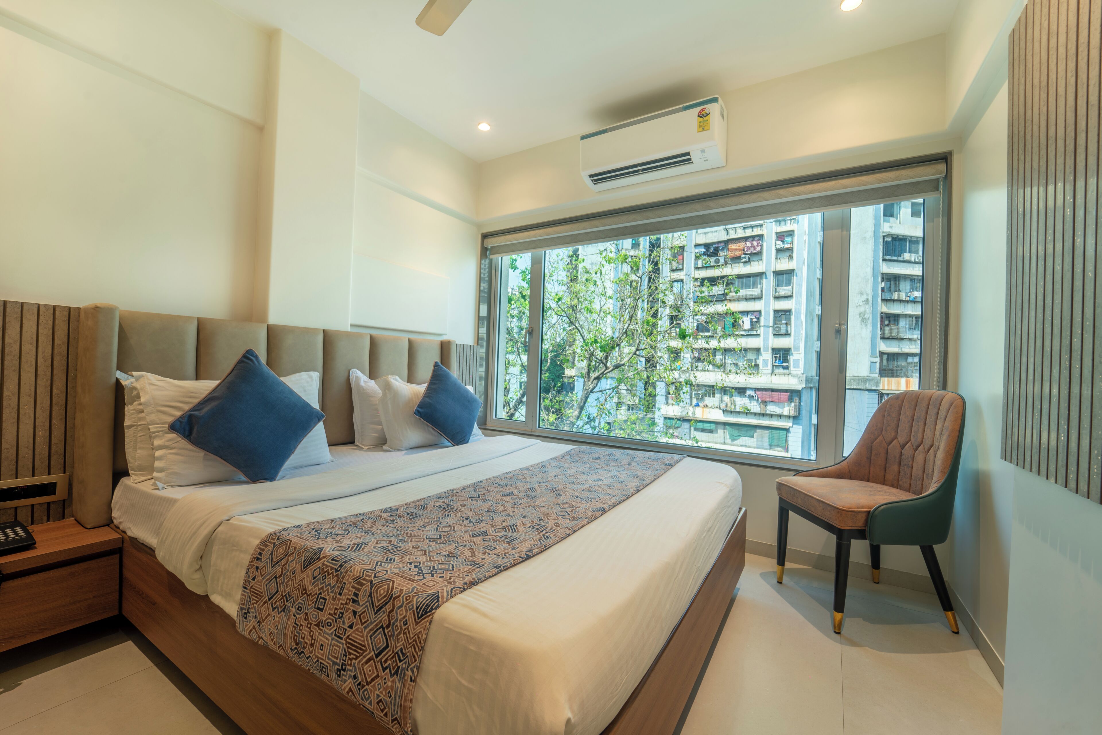 Une chambre d’hôtel moderne dotée d’un grand lit, d’une chaise, d’une fenêtre donnant sur la ville et d’un appareil de climatisation.